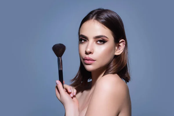 Young woman applies powder on the face using makeup brush. Beautiful girl doing contouring apply blush on cheeks. Face beauty cosmetics. Fresh skin and natural make up. Powder blush on facial skin