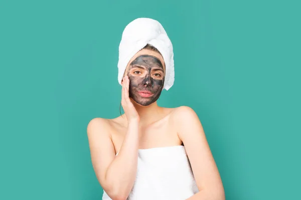 顔のマスク スキンケア 青いスタジオの背景に隔離された黒い粘土マスクを適用する女性 若いスパモデルはフェイスケアクリームを使用しています フェイシャルクリーム 保湿リフティング栄養クリーム — ストック写真