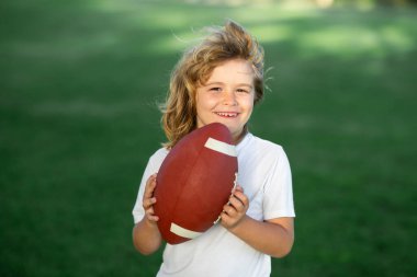 Sporcu çocuk. Amerikan futbolu ya da parkta rugby oynayan Amerikalı bir çocuk. Sportif çocuklar. Futbolcu topu tutuyor