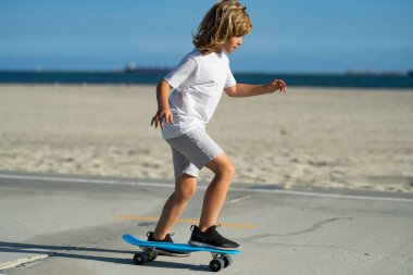 Kid boy riding skateboard in the road. Kid practicing skateboard. Children learn to ride skateboard in a park on sunny summer day. Active leisure and outdoor sport for child