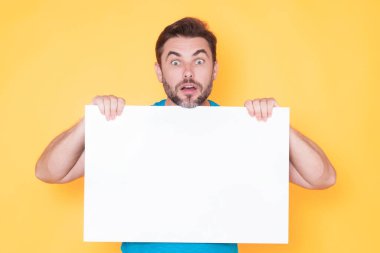 Boş tahtayı tutan ve stüdyo arkaplanını işaret eden yakışıklı, hayret verici adam. Kopyalama alanı olan boş tabela gösteren harika bir adam. Fikir ve teklif. Reklamınız. Boş reklam panosu