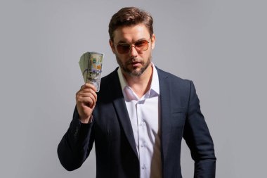 İşadamı, gri stüdyonun izole edilmiş geçmişini araştırıyor. Dolar banknotları olan takım elbiseli zengin bir adam. Dolar banknotları olan başarılı bir iş adamı. Takım elbiseli zengin milyoner
