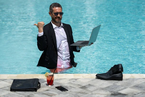 Leisure weekend and remote freelance work. Crazy comic business. Funny businessman in suit with laptop in swimming pool water. Remote summer work. Businessman relaxing in a swimming pool in a suit
