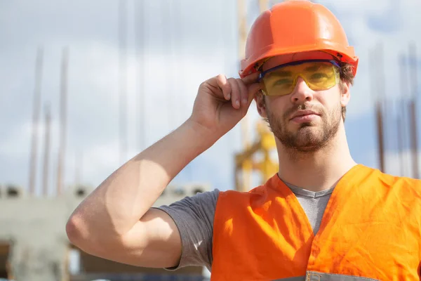 Man builder worker in helmet posing on construction site. Improvement and renovation. Brutal man builder. Engineer builder in uniform