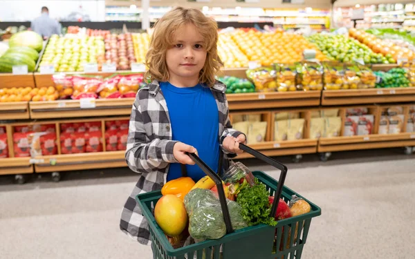 Child with shopping basket with grocery. Kid buying groceries in supermarket. Boy in shop. Concept of shopping at supermarket. Shopping with grocery cart. Grocery store, shopping basket