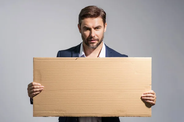Serious man holds the sign, blank card. Placard ready for your product. Sign to your text. Handsome man showing blank sign board over studio background. Empty blank board. Area advertising