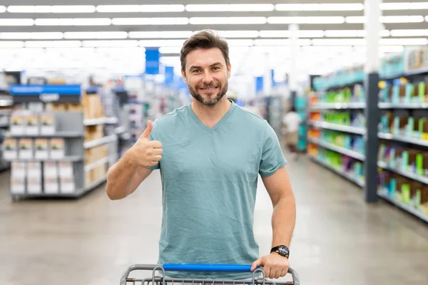 Handsome man hold shopping cart. Man holds shopping trolley. Store, shopping, sales and discounts. Male shopper. Man with shopping trolley at store