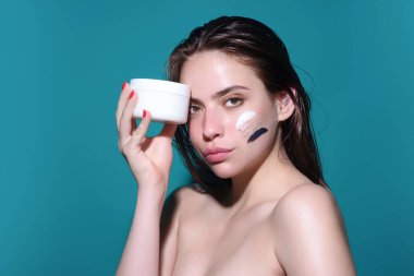 Beautiful model applying cosmetic cream treatment on face. Facial treatment. Beauty portrait of young topless woman with bare shoulders applying face cream