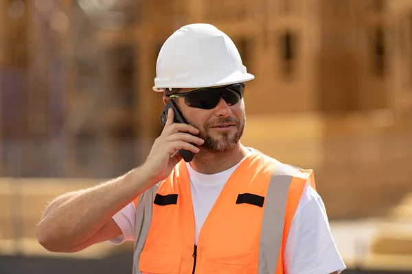 一个戴硬礼帽拿着电话打给更大的人 戴头盔的建筑工人建筑业的工人 工程师建造室外肖像 建筑工地的工人 — 图库照片