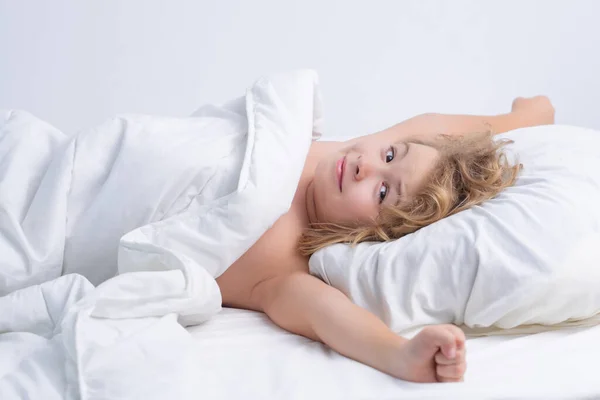 子供が目を覚ますとストレッチ 手を上げた ベッドでかわいい目覚めの子供 就寝時間 子供時代と成長の子供のコンセプト クローズアップ屋内肖像画 ベッドの中で面白い笑顔の子供 — ストック写真