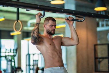 Spor salonunda poz veren kaslı iri kıyım. Spor aletlerinin yanında fitness mankeni. Genç kaslı adam egzersizi. Spor salonundaki güçlü kaslı adam. Spor ve motivasyon. Ağırlıkla egzersiz yapar