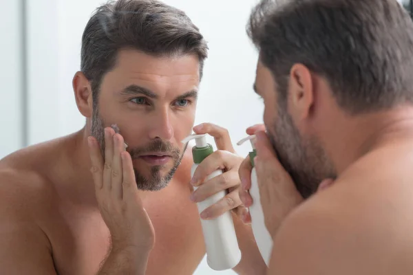 Male model applying cosmetic cream on face. Facial treatment. Beauty portrait of man applying face cream. Skin care product. Moisturizing creme for wrinkle face skin. Perfect skin, morning routine