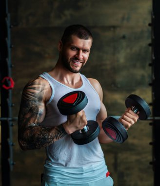 Muscular man workout in the gym. Athletic man having weight training in gym. Handsome man with strong muscles workout in the gym. Portrait of sexy muscular male with dumbbells. Bodybuilder exercise