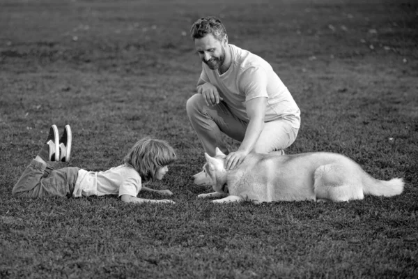 父と息子は夏の公園や庭で緑の芝生の上に座っています 家族旅行 ペットは友情と人々の概念が大好きです 週末のアクティビティ犬と幸せな家族 ペットフレンドとの子 — ストック写真