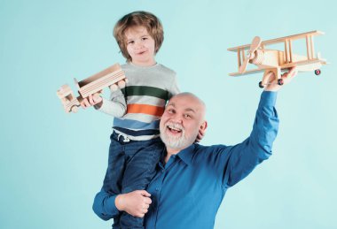Gelecek nesil aile rüyası. Mavi arka planda oyuncak uçağı olan mutlu büyükbaba ve torun izole edildi. Mutlu büyükbaba, torununu sırtında taşıyor.