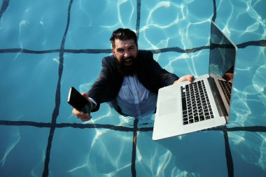 Yüzme havuzunda telefon ve laptop kullanan takım elbiseli komik sakallı bir iş adamı. Mobil cihazlarda çalışan gençlerin kavramı