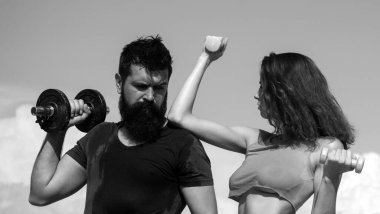 Dışarıda dambılları olan sağlıklı bir çift atletik erkek ve kadın. Dışarıda spor yapan bir çift. Genç fitness çifti, afiş. Spor mankenleri kollarını dambılla şişiriyor.