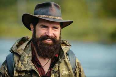 Kovboy şapkalı gezgin sakallı adamın portresi. Kırsalda gülümseyen mutlu orta yaşlı bir adamın portresi.