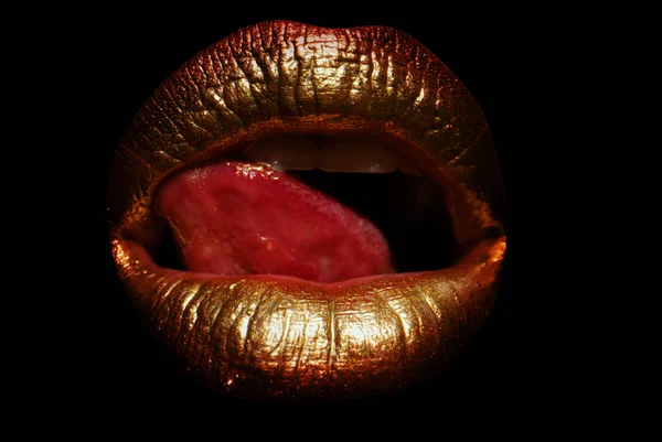 Golden lips with creative art gold metallic lipstick. Gold paint on lips of sexy girl. Sensual woman mouth, isolated background. Tongue lick golden lips. Glamour background. Lips icon