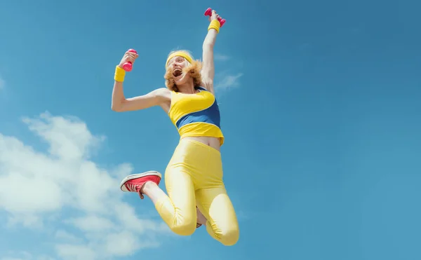 ダンベルと一緒にジャンプするスポーティ女性 空を背景にスポーツウェアを着た面白い女性 ダイナミックな動きだ スポーツと健康的なライフスタイルフィットネス女性 — ストック写真