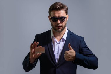 Elinde kredi kartı tutan yakışıklı bir adam. Gri stüdyo geçmişinde kredi kartı olan orta yaşlı bir adam. Kredi kartı konsepti. Takım elbiseli bir işadamı kredi kartıyla ödeme yapıyor.