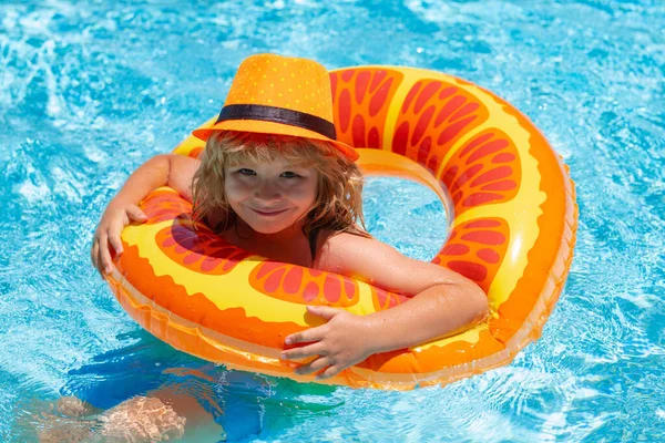 Child swimming in pool play with floating ring. Smiling cute kid in sunglasses swim with inflatable rings in pool in summer day. Fashion summer kids hat
