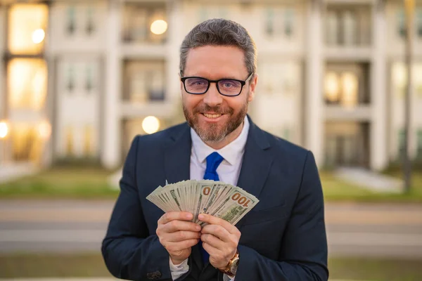 Man in suit holding cash money in dollar banknotes outdoor. Portrait of businessman with bunch of dollar banknotes. Dollar money concept. Career wealth business. Insurance agent