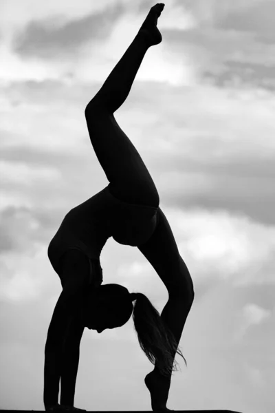 Girl gymnastic silhouette on sky. Young slender girl doing acrobatic stunt. Gymnast in backlight