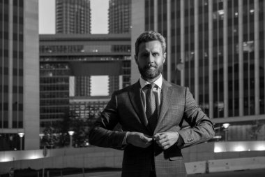 Modern ofis binasının yakınında kendine güvenen bir erkek yönetici. İşadamı ayağa kalkar ve gece şehir geçmişi
