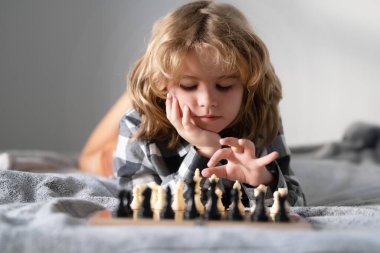 Çocuk satranç oynuyor. Satranç tahtasının yanında çocuk düşüncesi. Öğrenmek ve büyütmek, çocuk büyütmek. Çocuklarla evde satranç oynamak
