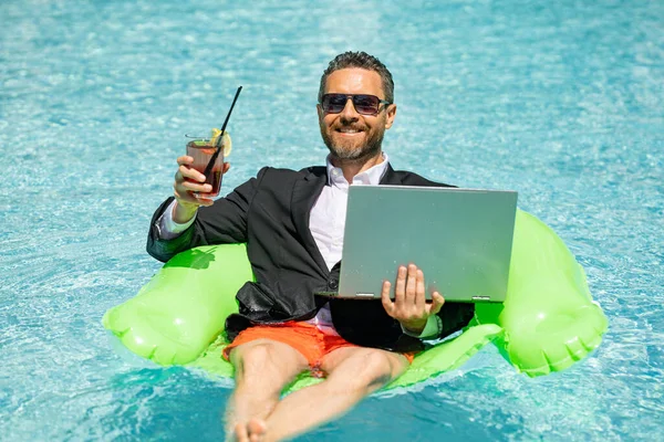 Summer business dreams. Millennial business man in suit floating with cocktail and laptop in swimming pool. Summer vacation. Funny crazy businessman rest in formal wear in pool. Hot summer business
