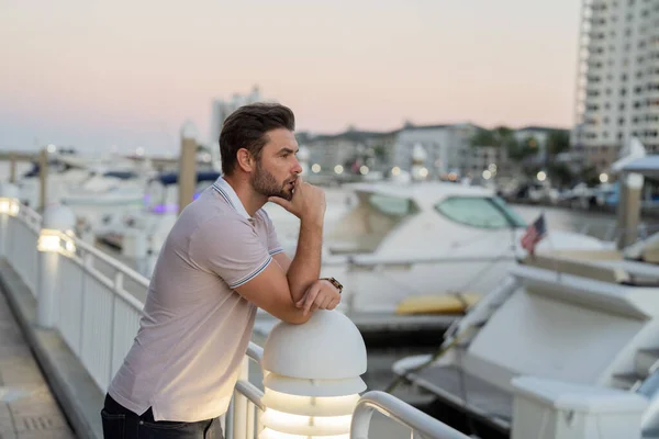 Rich business man dreaming and thinking near the yacht. Successful male model in big city living the urban lifestyle. Young male fashion model walking in street. Young hispanic man at the street