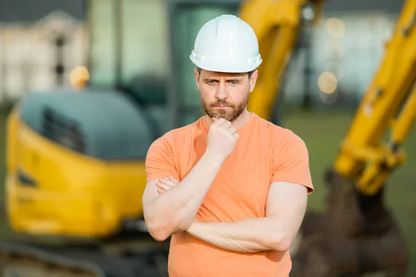 Worker in helmet on site construction. Excavator bulldozer male worker. Construction driver worker with excavator on the background. Construction worker with tractor or construction at building