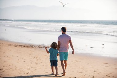 Baba ve oğul yaz plajında yürüyor. Yaşam tarzı ve aile tatili, mutluluk adamı konsepti.