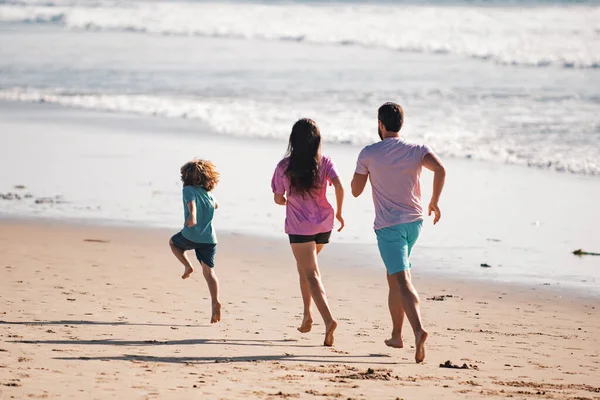 幸せな家族の父 母と赤ちゃんの息子が一緒に楽しみを持って 黒砂のビーチで海の波に沿って水プールで実行されます 夏休みに子供と一緒に旅行ライフスタイル — ストック写真