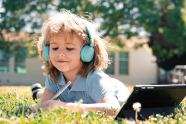 Küçük öğrenci okul parkında defter ya da tablet kullanıyor ve nomework yazıyor. Sağlıklı okul çocuğu