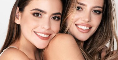 İki seksi kızın kadın yüzü, yakın plan. Doğal güzellik ve cilt bakımı. Kozmetik ve makyaj malzemeleri. Genç, mutlu, sarışın ve çıplak omuzlu esmer kadınların güzel portresi.