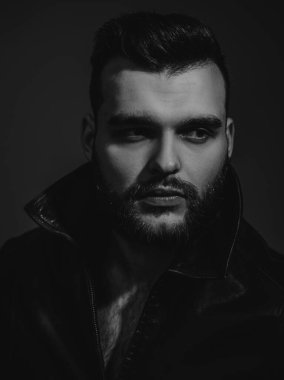 Yakışıklı bir gencin portresi. Eski moda kıyafetler, eski moda deri ceket. Erkeklik kavramı. Saç stili olan vahşi sakallı motorcu. Çekici erkek.