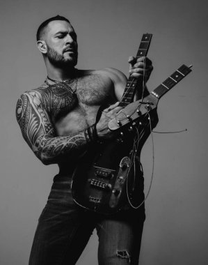 Müzik dükkanı. Yetişkinler için öğrenme ve çalma müziği. Müzik ve DJ konsepti. Sakallı, stil sahibi, vahşi bir adam, bir dövme gitarda bir oyunu taklit ediyor. Tıraşsız, konsantre bir adam. Bir erkeğin seksi görünüşü.