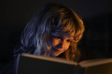 Kitap okuyan şirin bir çocuk. Açık kitabı olan bir çocuk. Ev okulu dersi. Evde kitap okumaya odaklanmış küçük bir çocuk. Yatmadan önce masal masalı