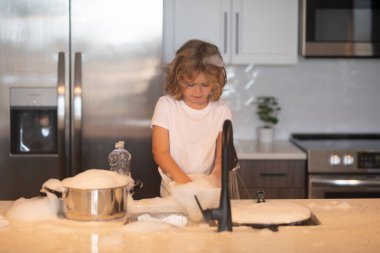 Evde bulaşıkları yıkayan 7-8 yaşlarında bir çocuğun portresi. Mutfakta bulaşık yıkamada çocuk yardımı