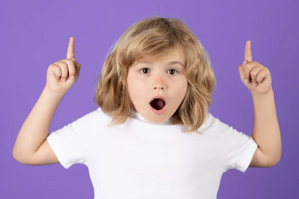 Surprised child pointing up finger on isolated studio background. Shocked kid pointing to copyspace, showing promo offers, points away. Excited emotions, shock, omg and wow expression