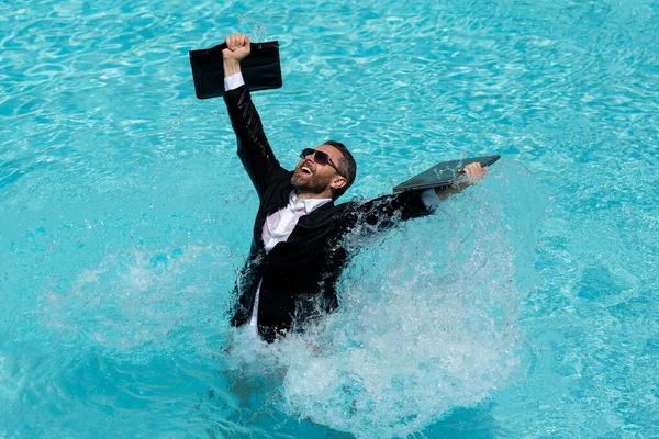 Summer weekend and remote freelance work. Crazy comic business. Funny businessman in suit with laptop in summer swimming pool water. Remote summer work. Businessman relaxing in a pool in a suit