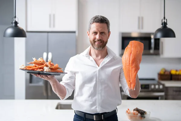 Chef man cooking seafood crab and shrimp, salmon and lobster in kitchen. Cook on kitchen with salmon fillet. Salmon recipes. Baked salmon fillet