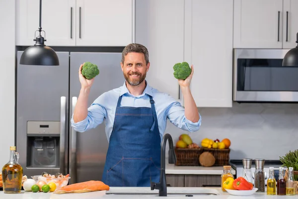 コックエプロンのヒスパニック系の男は台所でブロッコリーを保持します キッチンで野菜を調理するシェフエプロンのハンサムな男 サラダボウルで男を食事 グリーンサラダ健康食品のコンセプト — ストック写真