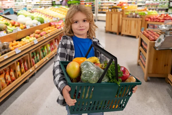 Portrait of child with shopping cart full of fresh vegetables in a food store. Supermarket shopping and grocery shop concept. Shopping kids. Child buying grocery in supermarket. hold shopping basket