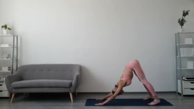 Genç sporcu kadın yoga egzersizi yapıyor. Ev antrenmanı. Spor giyimli, spor kıyafetli, uzun boylu bir kadın. Mutlu milenyum kızları odada yoga minderinde spor yapıyor. Sağlıklı yaşam tarzı kavramı