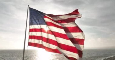 4 Temmuz. Ulusal Amerikan Bağımsızlık Günü kutlaması. Amerikan Bayrağı. Amerikan bayrağı dalgalanıyor, deniz ve günbatımı yakınlarında. ABD bayrağı dalgalanan bayrak direği