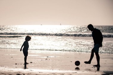 Baba ve oğul yaz tatillerinde plajda futbol ya da futbol oynarlar. Baba ve çocuk gün batımında açık havada siluetin keyfini çıkarıyorlar.