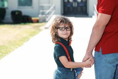 Öğretmenlerin elini tutan mutlu inek öğrenci portresi. Okullu çocuk babamla aynı okula gidiyor. Okul kapısının önünde çocuklu bir ebeveyn